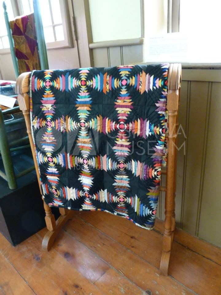 A black quilt with colourful fabric designs, hanging on a wooden rack