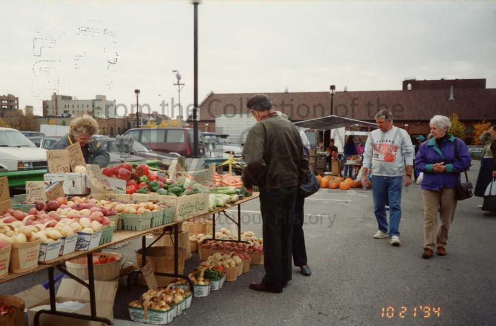 Colour photo of people shopping at a farmer's market, with a table full of produce.